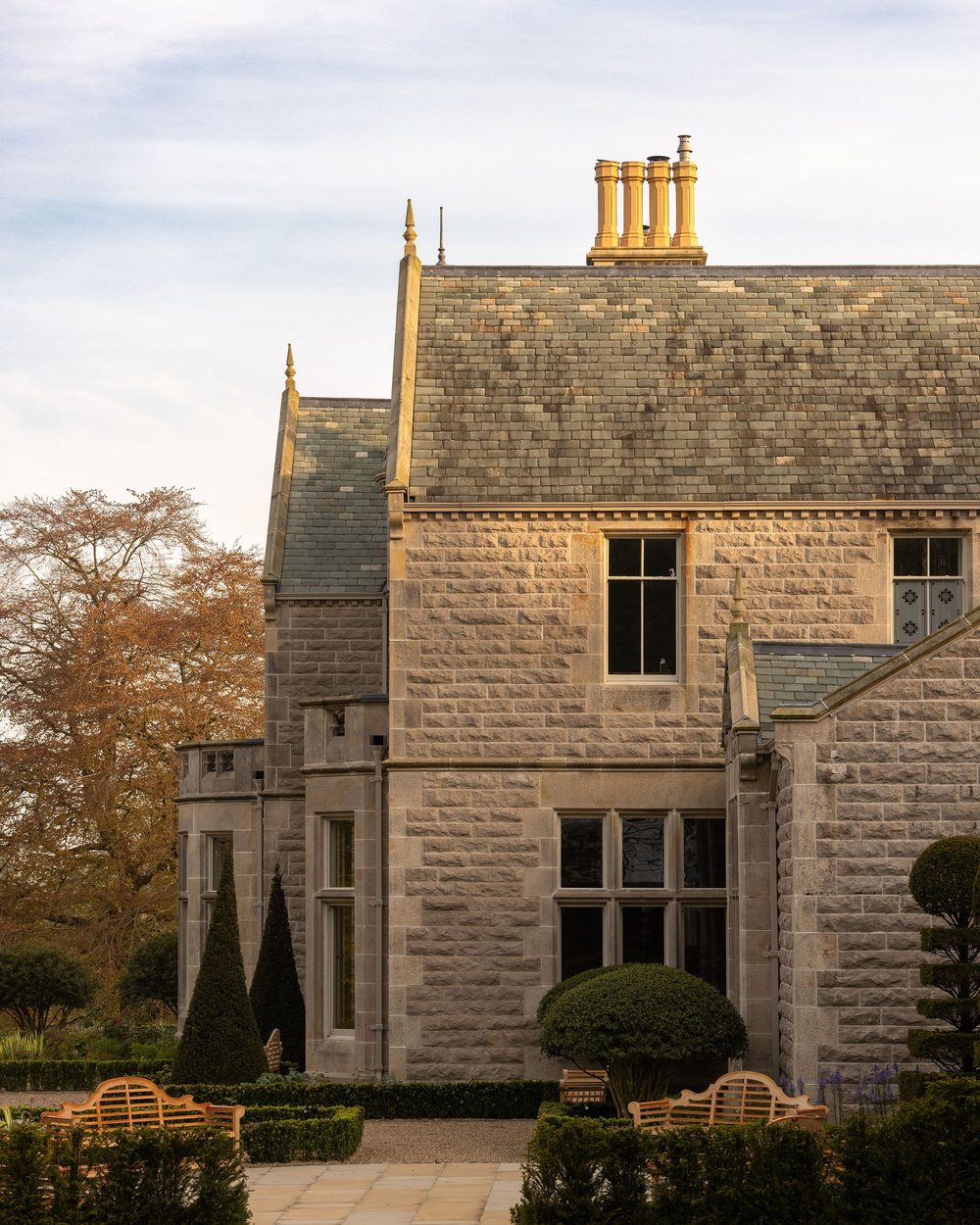 A stone country house with clipped hedges and a gravel path
